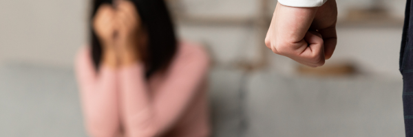 Photo shows a women hiding her face from a clenched fist