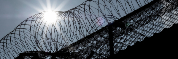 Photo shows rolls of barbed wire on top of a prison fence